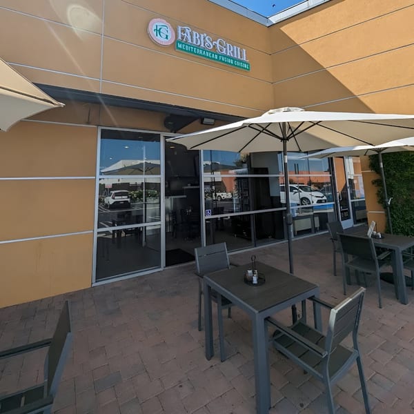 Fabi's Grill Mediterranean Fusion Cuisine storefront with outdoor patio seating and umbrellas on a sunny day.