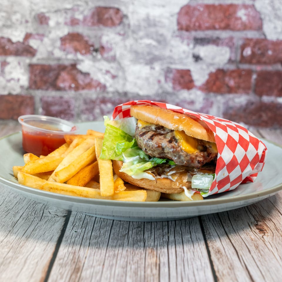 A Fabi's Grill burger with cheese, lettuce, and sauce, wrapped in checkered paper, served with fries and ketchup.