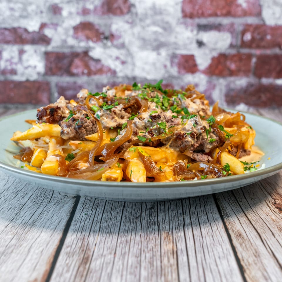 Fabi's Grill loaded fries with meat, caramelized onions, cheese sauce, and parsley on a plate.
