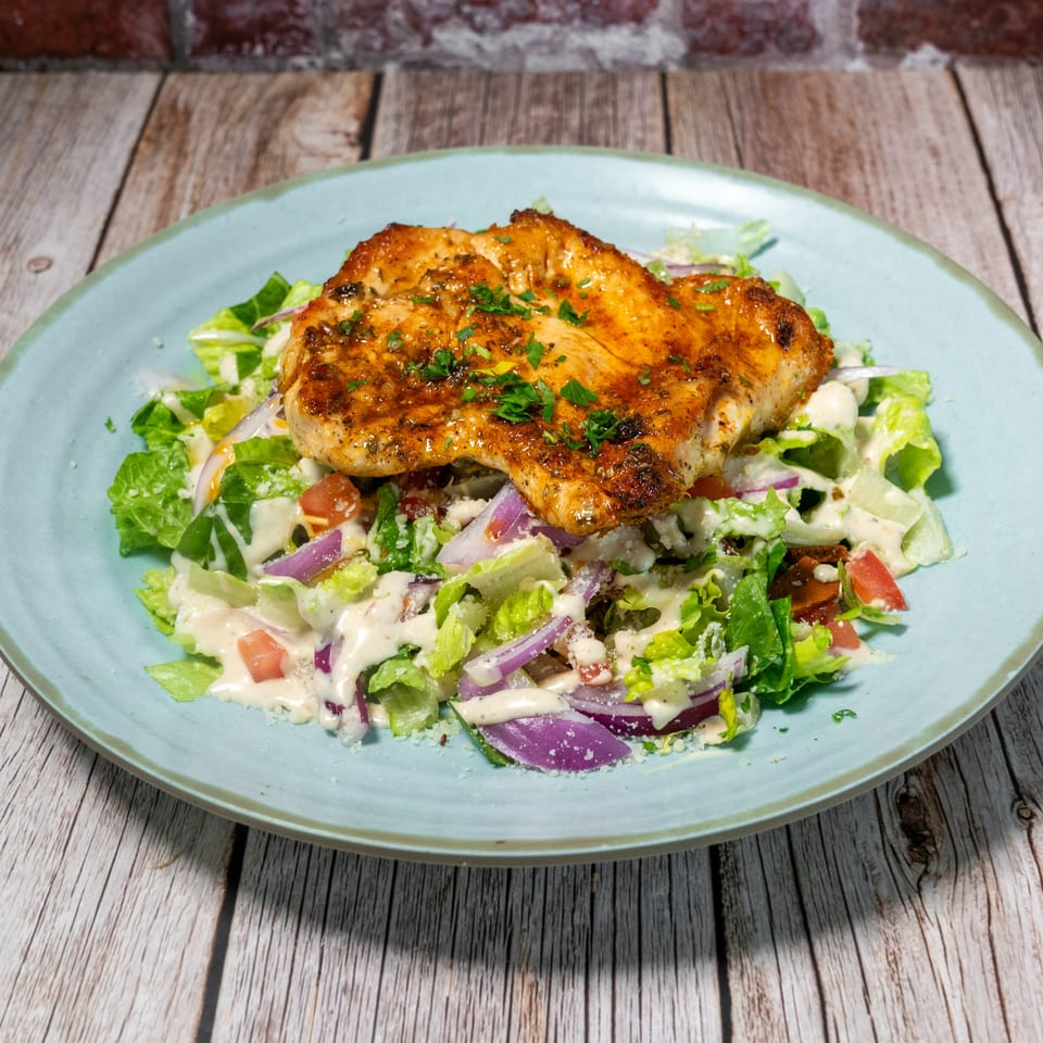 Grilled chicken breast on a fresh Mediterranean salad with dressing, red onions, and tomatoes.