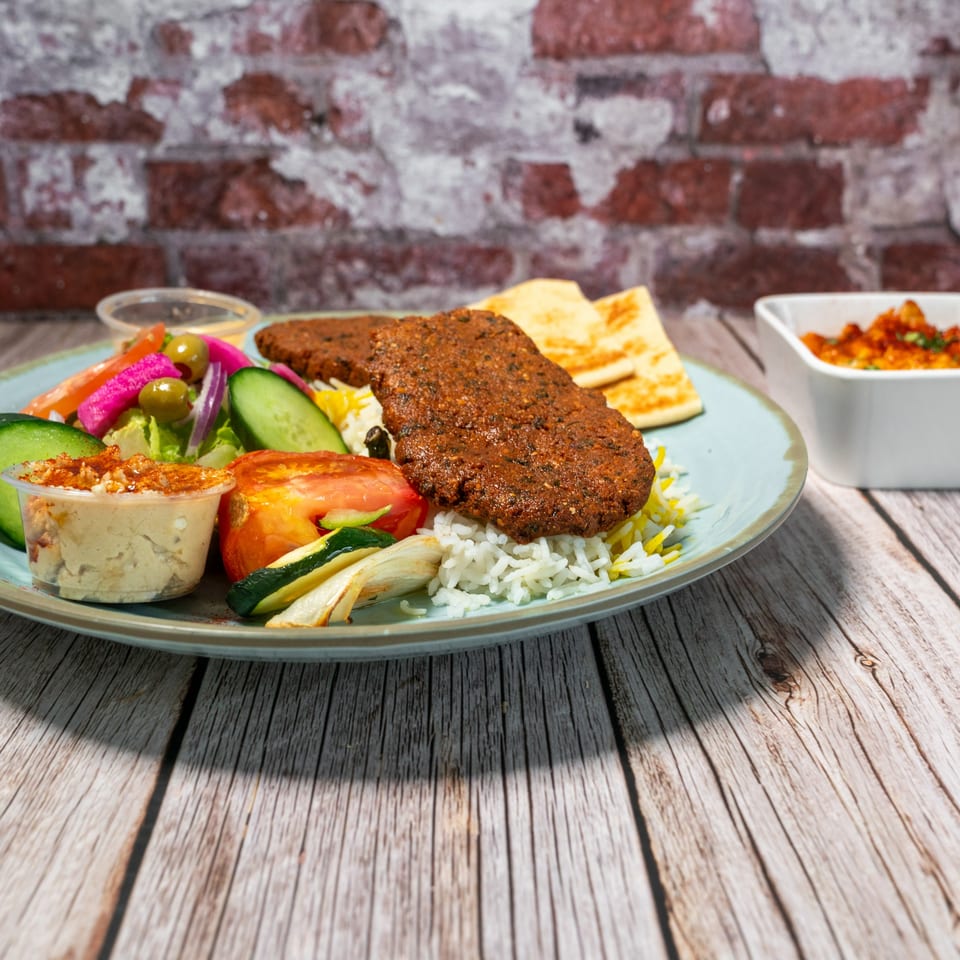 Mediterranean platter with grilled meat, rice, hummus, salad, and pita bread on a wooden table.