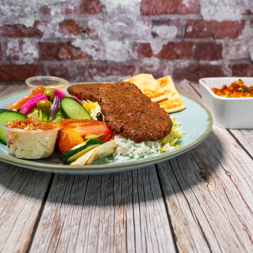 Mediterranean platter with grilled meat, rice, hummus, salad, and pita bread on a wooden table.