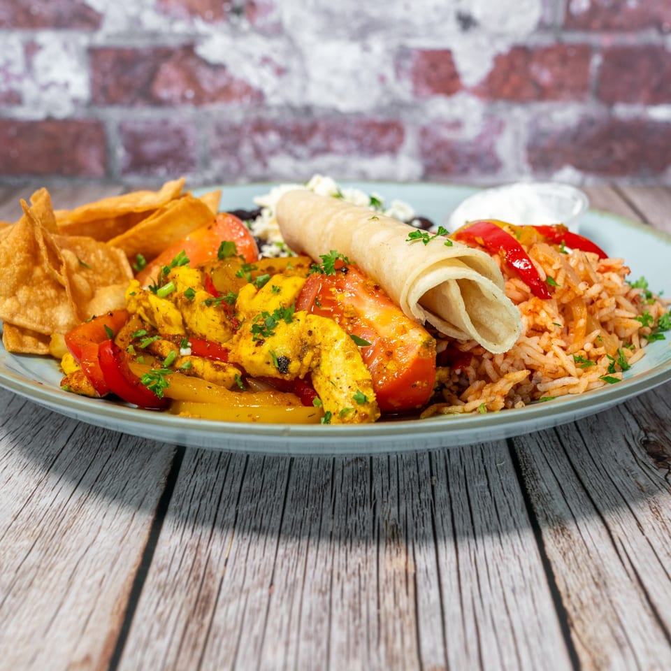 Fabi's Grill chicken fajitas with rice, beans, tortilla, chips, and sour cream on a light blue plate.