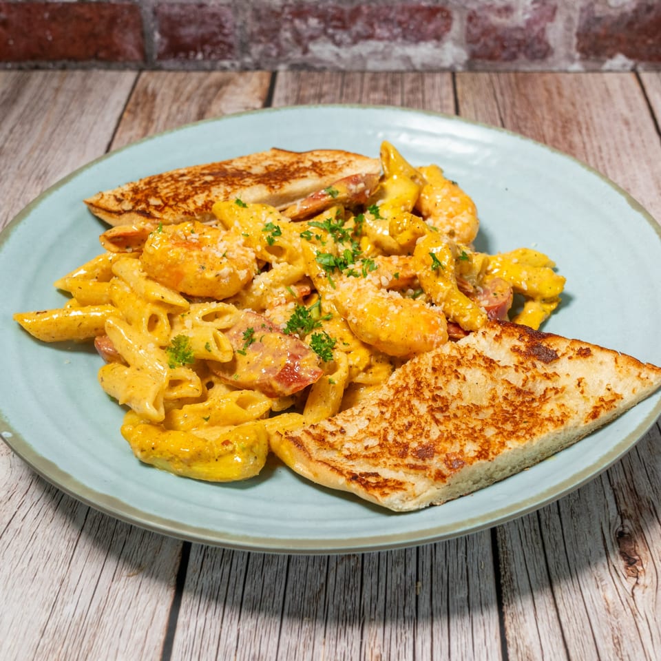 Creamy penne pasta with shrimp and sausage, garnished with parsley and parmesan, served with toasted bread.