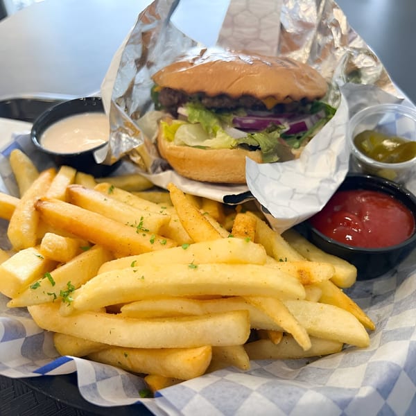 A Fabi's Grill burger with lettuce, onion, and cheese, served with fries, ketchup, and sauces.