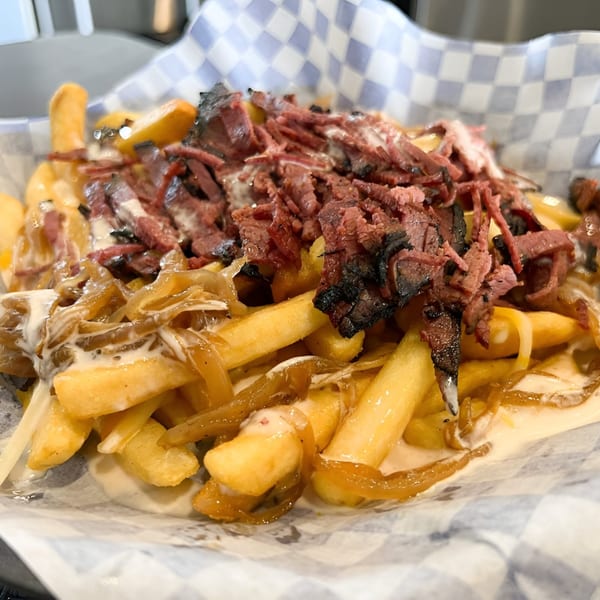Fabi's Grill loaded fries with pastrami, caramelized onions, and white sauce in a checkered paper-lined basket.