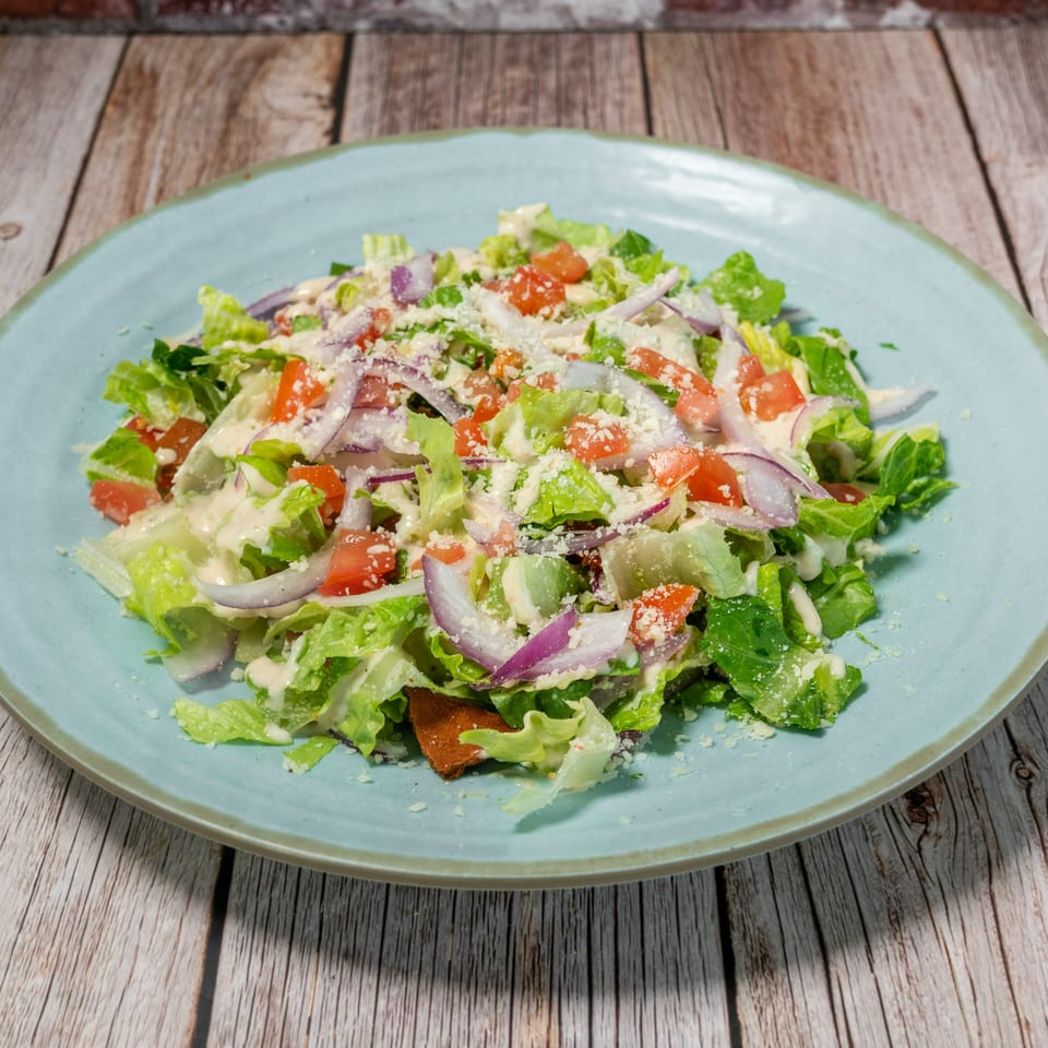 Fabi's Grill Mediterranean salad with lettuce, tomatoes, red onions, dressing, and grated cheese.
